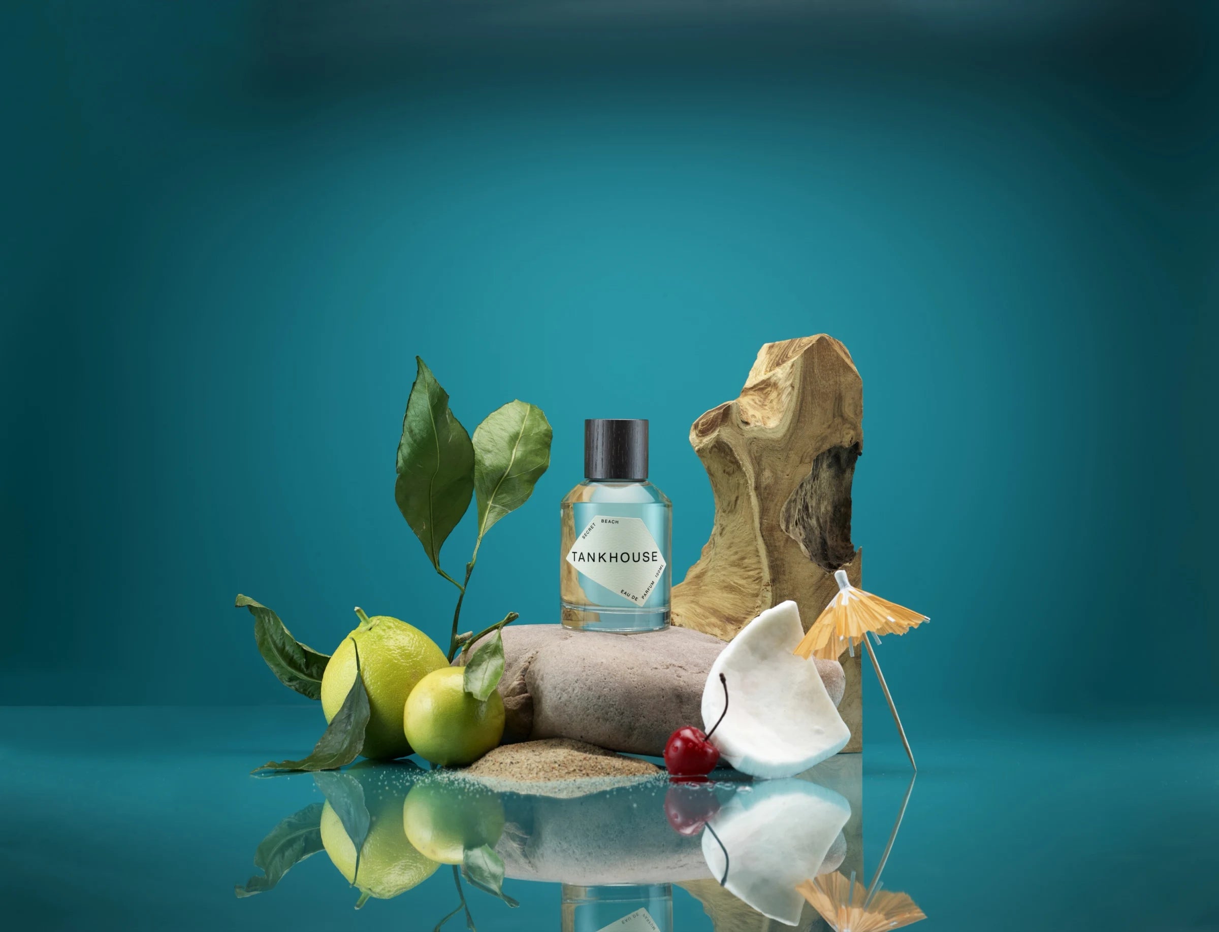 Secret Beach bottle staged with citrus, sand, driftwood, shell, and water reflections